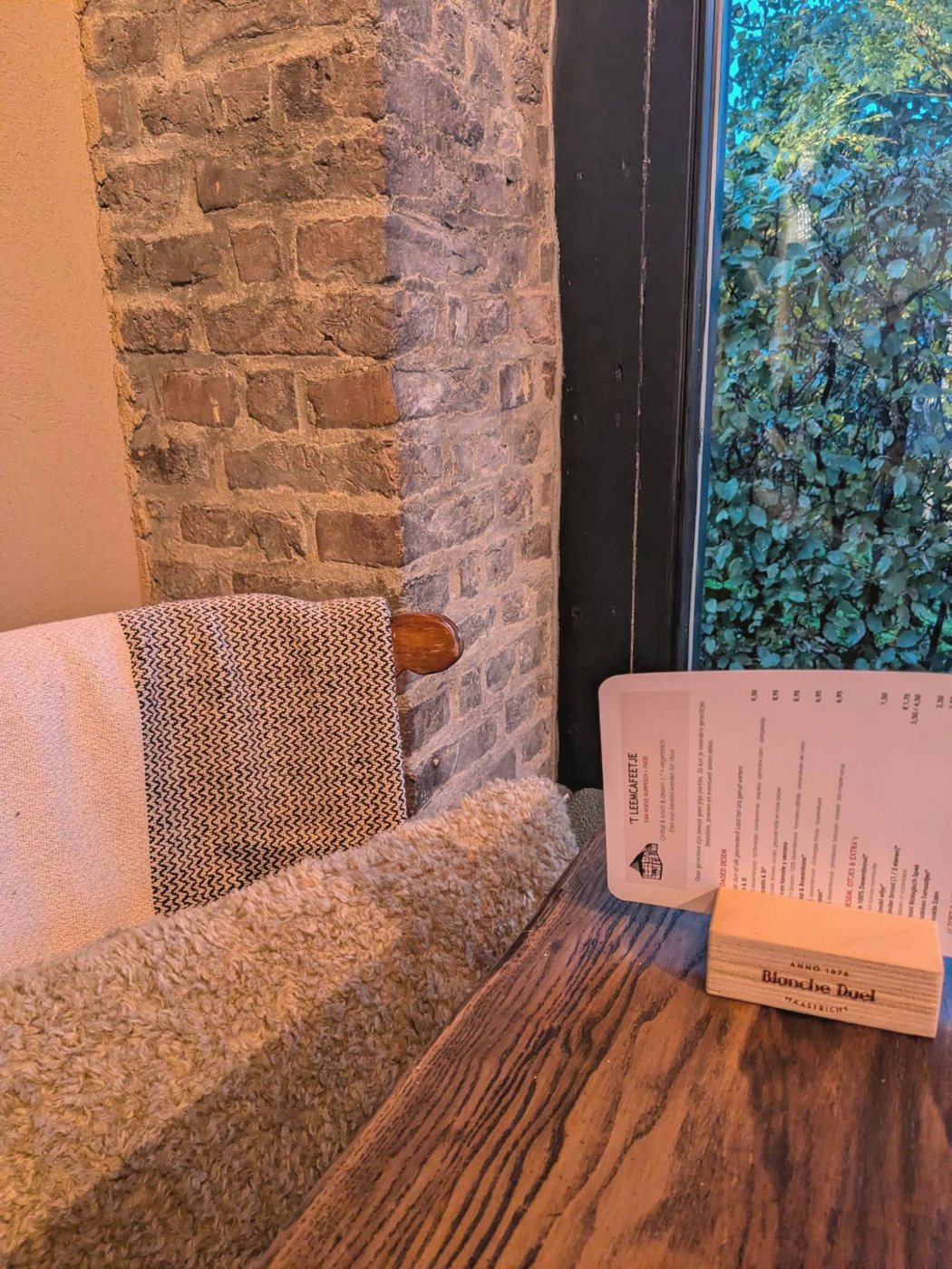 Menukaartje op een houten tafel naast een bakstenen muur